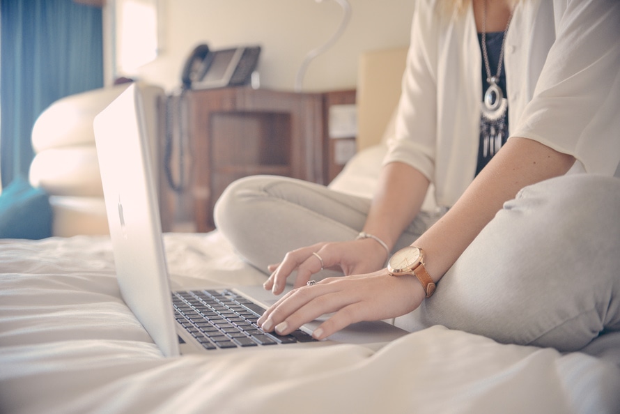 Woman typing on her laptop, sitting on her bed